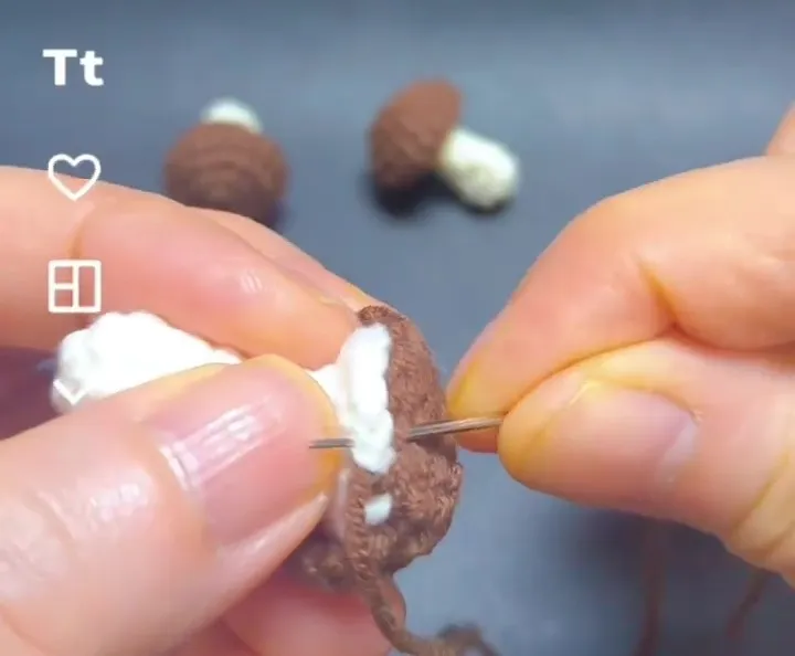 sewing the crochet mushroom stem to the cap with a yarn needle