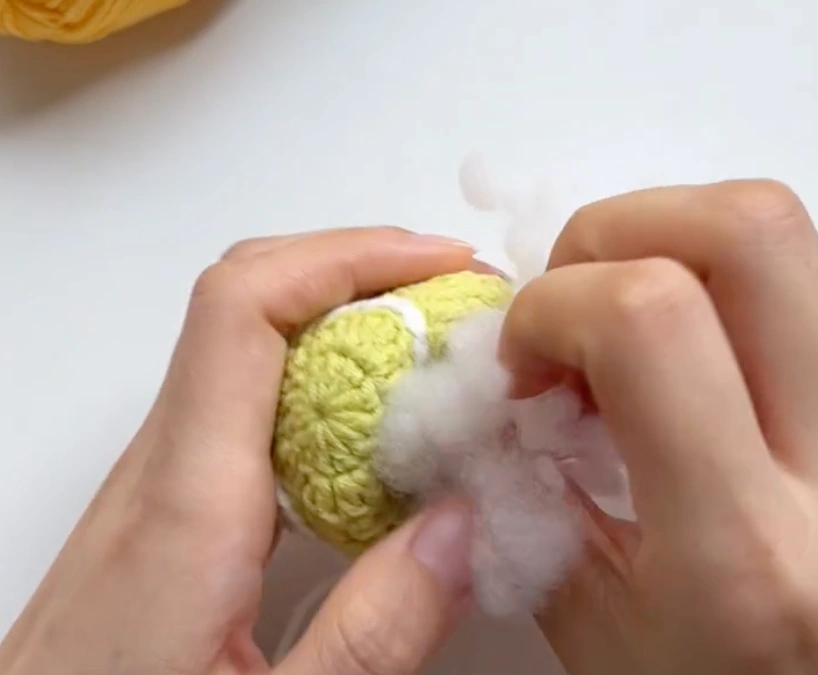 Fiberfill stuffing being added into a partially joined crochet tennis ball