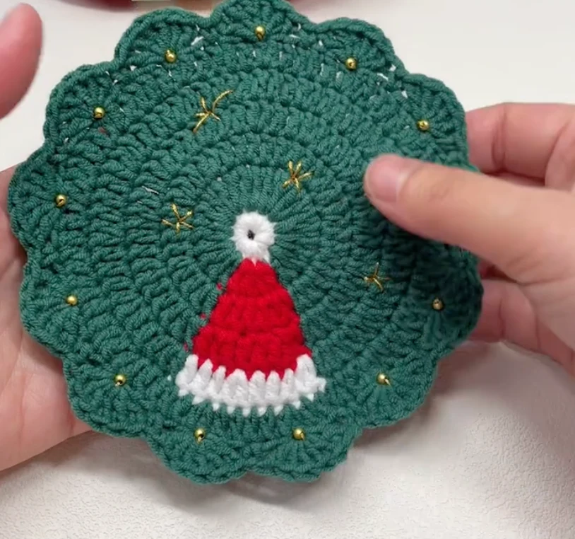 Santa Hat Crochet Coaster: A Festive Beginner Christmas Pattern 7 Finished Christmas hat crochet coaster with green scalloped edge, red Santa hat, white brim, and small gold details