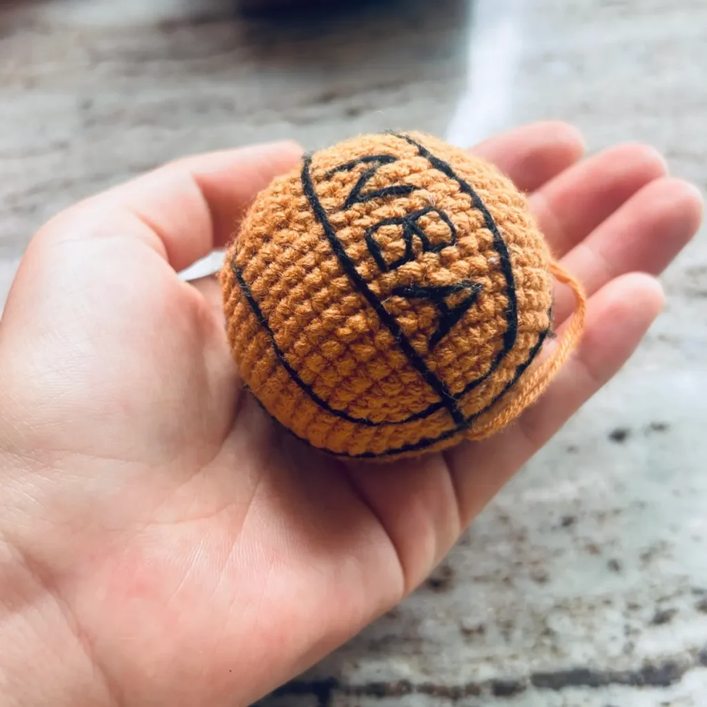 Finished mini crochet basketball held in hand with black embroidered lines