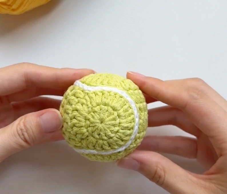 Finished mini crochet tennis ball with white curved seam