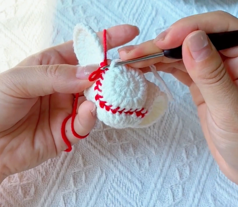 Red yarn joining two white crochet baseball panels together