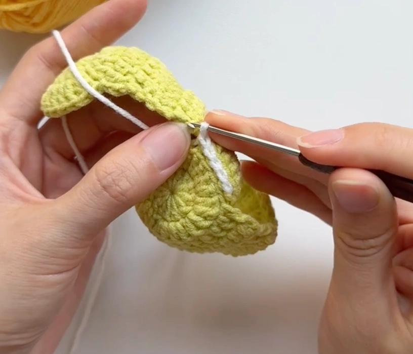 White yarn joining two crochet tennis ball panels together with a hook