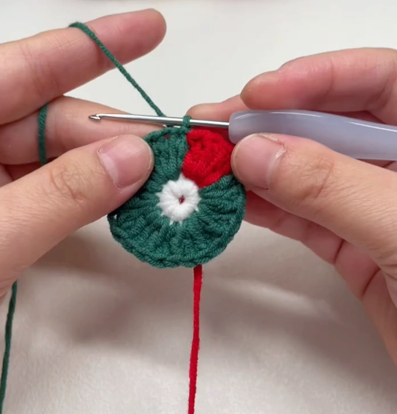 Santa Hat Crochet Coaster: A Festive Beginner Christmas Pattern 2 Early rounds of a crochet Santa hat coaster showing the red hat section starting beside the green background